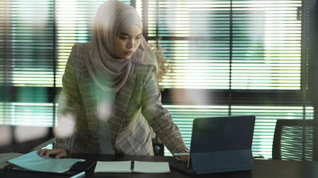 View through glass wall of young muslim businesswoman working with digital tablet in office roomの写真素材