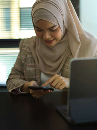 Portrait of Asian muslim businesswoman using smartphone while working with tablet in officeの写真素材