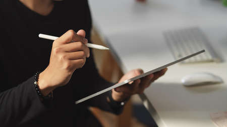 Close up view of male hand using digital tablet while sitting at workplace