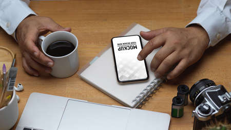 Top view of male hand using smartphone and holding coffee mug on workspace, include clipping path
