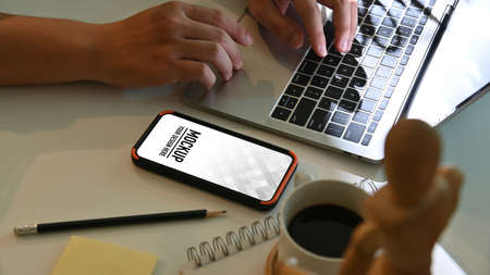 Side view of male hands typing on laptop keyboard on white table with smartphone, include clipping...