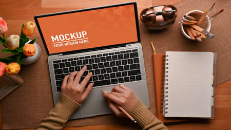 Top view of female hands typing on laptop keyboard on the table with notebook, stationery and...