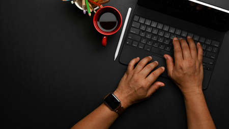 Top view of male hands typing on tablet keyboard on black table with coffee cup and copy spaceの写真素材