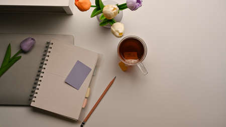 Top view of feminine workspace with notebook, laptop, coffee cup, flower vase and copy space