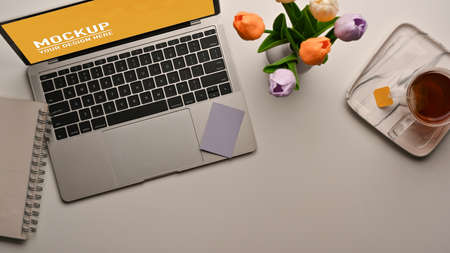 Top view of workspace with laptop, notebook, flower vase and tea cup on the table