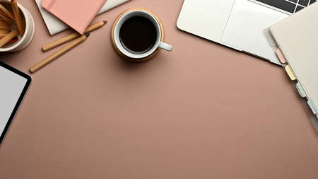 Top view of workspace with digital devices, stationery, coffee cup and copy space on pink tableの写真素材