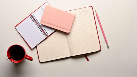 Top view of opened blank notebooks, pencil and coffee mug on white table in home office room