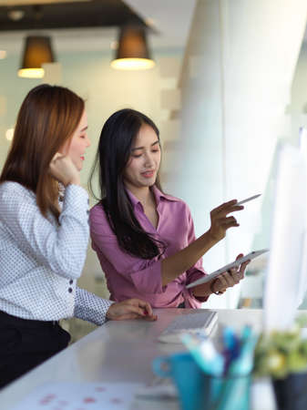 Portrait of two businesswomen working together with computer device in office roomの写真素材