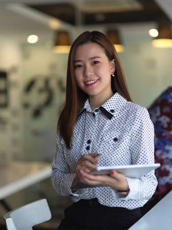 Portrait of female office worker holding tablet while sitting in office room