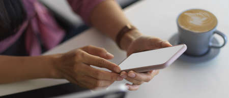 Side view of female hands using smartphone on white table with coffee cup and tablet, clipping path