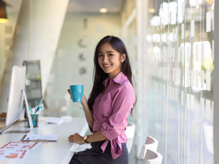 Portrait of businesswoman smiling to camera while take a coffee break in office room