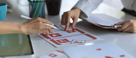 Close up view of two UI designers consulting on their project with paperwork and supplies