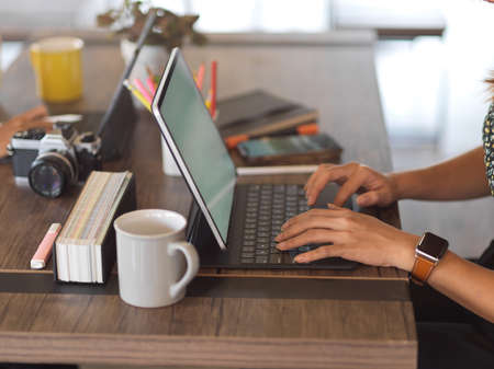 Side view of female hand working with laptop on wooden worktable in office room