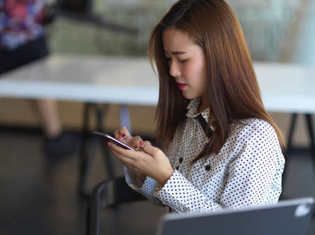 Side view of businesswoman using smartphone while relaxing in office roomの写真素材