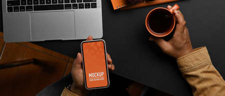 Top view of male hand using smartphone and holding coffee cup on worktable, include clipping pathの写真素材