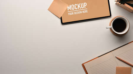 Top view of workspace with tablet, notebook, coffee cup and copy space on white table