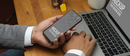 Close up view of businessman hand holding smartphone while working with laptop, include clipping...