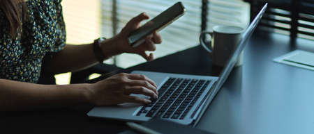 Side view of female hand using with laptop and smartphone on worktable in office room