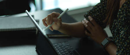 Cropped shot of female hand holding stylus pen to work with digital tablet on worktable