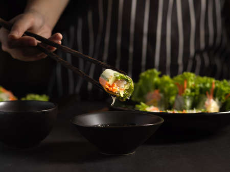 Close up view of female cook gripping  Vietnamese spring rolls with chopstick in dark backgroundの写真素材