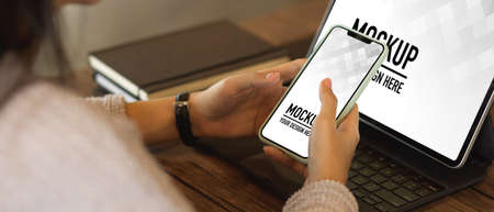 Close up view of female using smartphone while working with digital tablet in office roomの写真素材