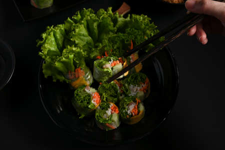 Top view of female cook gripping  Vietnamese spring rolls with chopstick in dark background