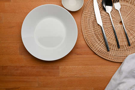Top view of dinning table with mock up ceramic plate, cutlery, place mat and copy space