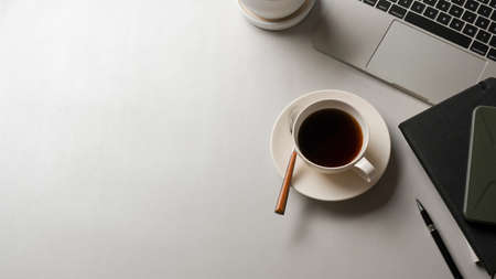 Top view of white table with coffee cup, laptop, stationery and copy space in office room