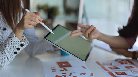 Close up view of two UI developers meeting on their project with paperwork and tablet on meeting...