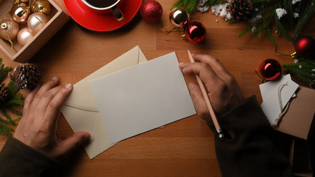 Top view of male hands writing greeting card on wooden table decorated with Christmas decorationsの写真素材