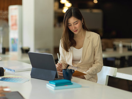 Portrait of businesswoman working with schedule book and tablet on worktable in cafeteriaの写真素材