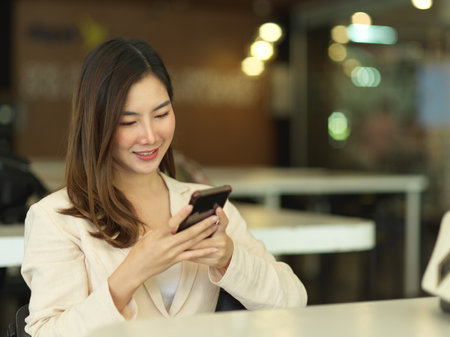 Portrait of businesswoman relaxing with smartphone while sitting in cafeteriaの写真素材