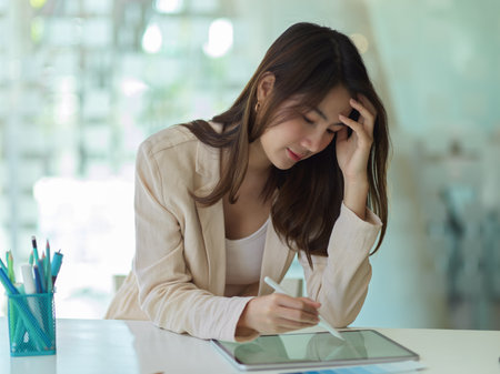 Portrait of businesswoman feeling tried while working with tablet in office roomの写真素材
