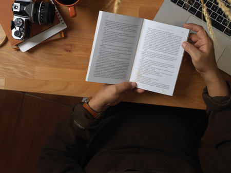 Top view of male reading book on wooden worktable in home office room