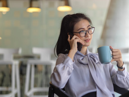 Close up view of businesswoman talking on the phone while take a break with coffee in office roomの写真素材