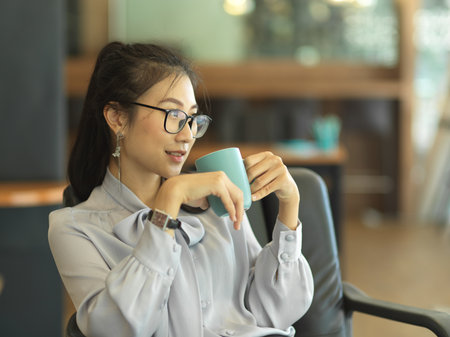 Portrait of businesswoman drinking coffee while relaxing  in office roomの写真素材