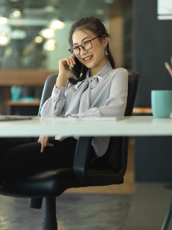 Portrait of businesswoman talking on the phone while sitting in modern office roomの写真素材