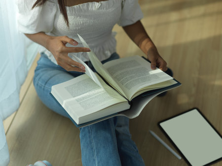 Top view of female reading a book while relaxed sitting on the floor with tablet in living roomの写真素材