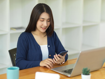 Portrait of businesswoman working with smartphone and laptop on worktable in office roomの写真素材