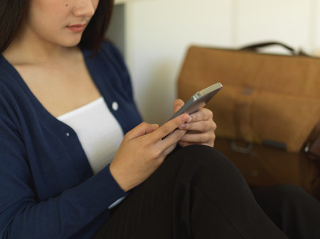 Cropped shot of female using smartphone while relaxed sitting in libraryの写真素材