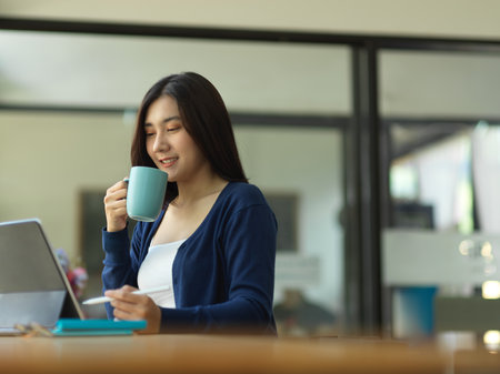 Portrait of businesswoman drinking coffee while working with digital tablet in cafeの写真素材