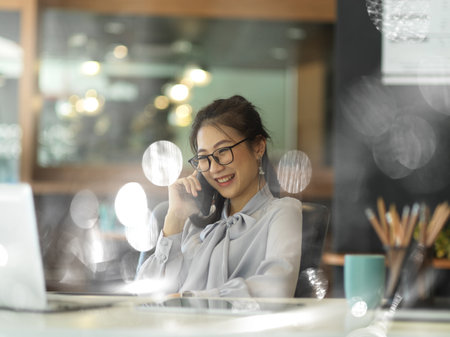 View through glass window of businesswoman talking on the phone in office roomの写真素材