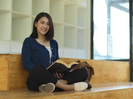 Portrait of female university student smiling to camera while reading a book in reading cornerの写真素材