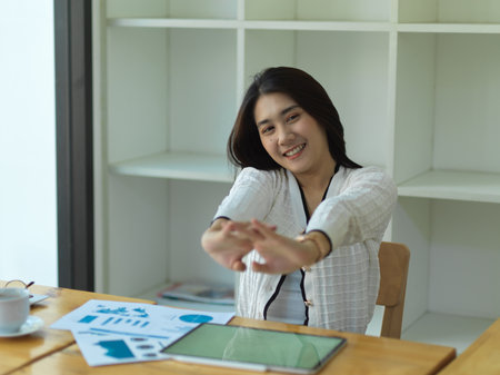 Portrait of businesswoman relaxing, stretching her arms while working in office roomの写真素材