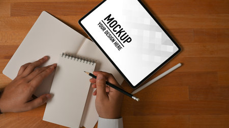 Top view of businessman working with tablet and blank notebook on wooden tableの写真素材
