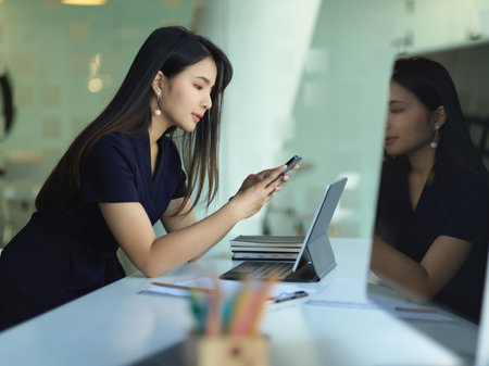 Side view of female office worker using smartphone while working in office roomの写真素材