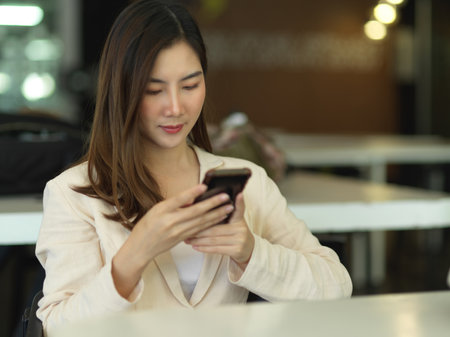 Portrait of female office worker using smartphone while relaxed sitting in cafeteriaの写真素材