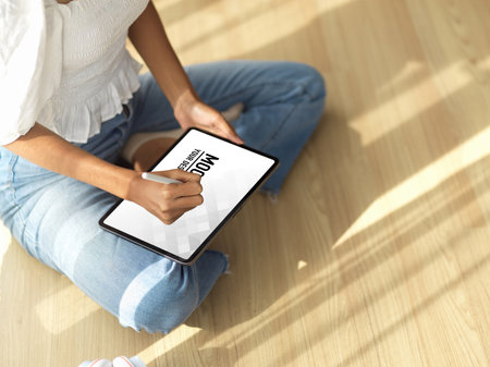Cropped shot of female teenager using digital tablet on her lap while legs crossed sitting on the floorの写真素材