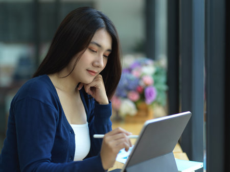 Portrait of female student doing assignment with tablet on wooden bar in cafeの写真素材