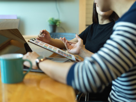 Side view of two designers discussing on their project with laptop and colour chart in office roomの写真素材
